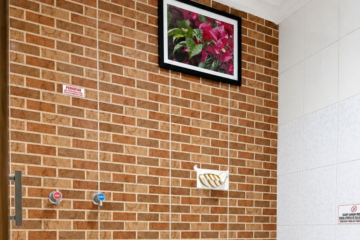 A bathroom with a brick wall, a toilet, a shower, and a picture of flowers.