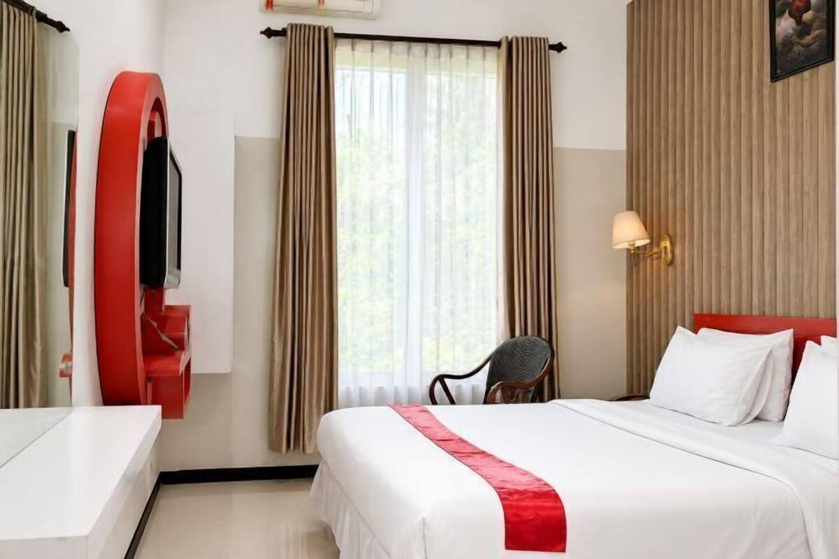 Una habitación de hotel con cama, una silla, un escritorio, un televisor y cortinas.