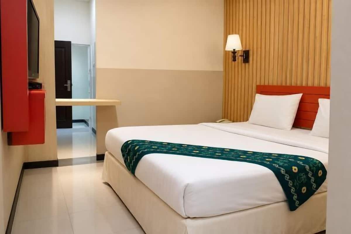 Habitación de hotel con cama, escritorio, televisión y lámpara de pared.