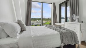 Una camera da letto con un letto grande, una cassettiera e vista sulla città attraverso ampie finestre.