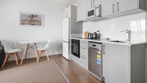 Una cucina moderna con mobili bianchi, un forno a microonde, un bollitore e una lavastoviglie. C'è un piccolo tavolo da pranzo con due sedie.