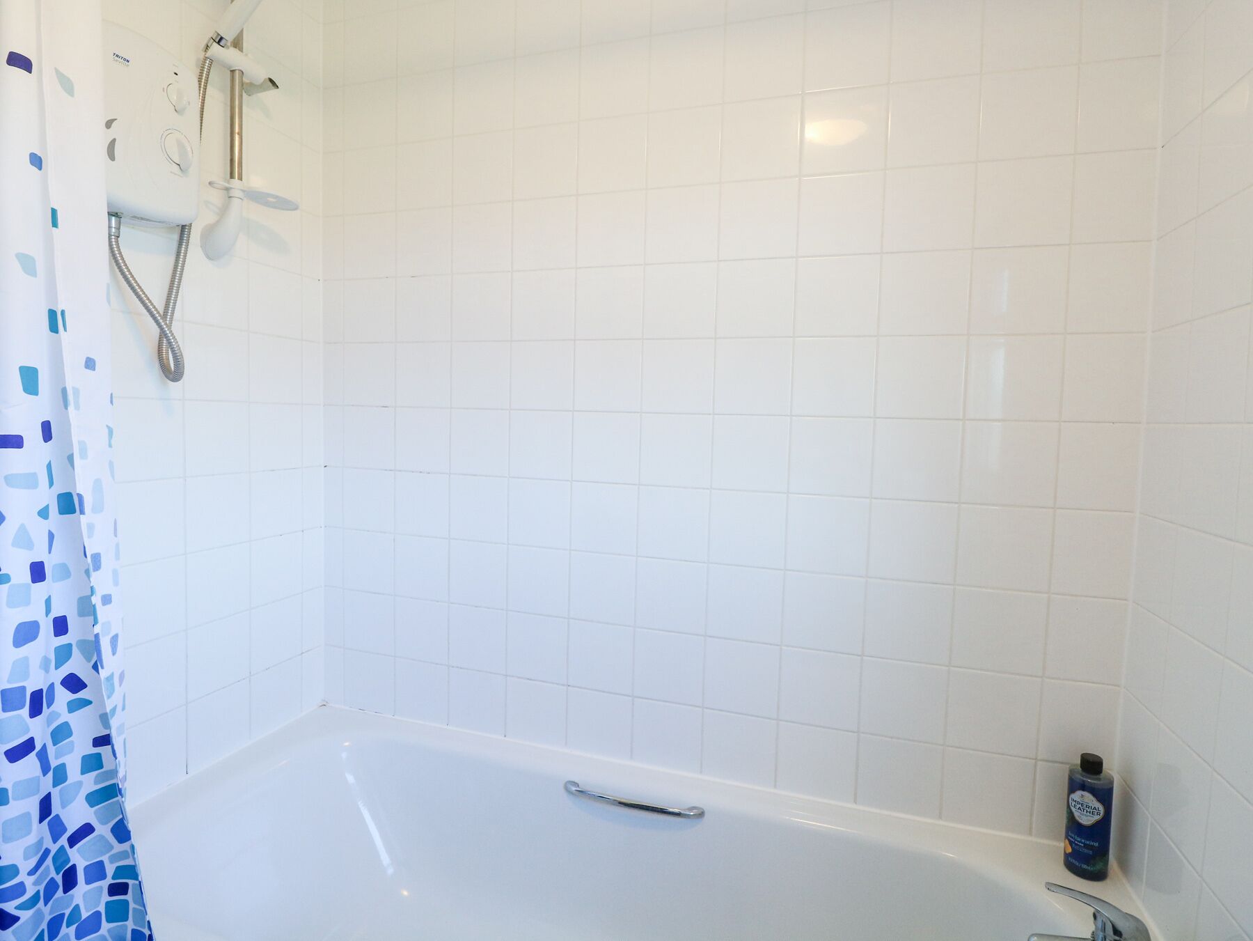 Een badkamer met een witte badkuip, een douche met een handdouche en een fles shampoo ernaast.