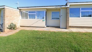 A two-story mobile home with a brick exterior, a small front yard, and a clear blue sky. - Chalet 38 (Great Yarmouth)