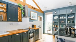 A modern kitchen with wooden cabinets, a built-in oven, and a large window. - The Barn (Riding Mill)
