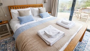 A neatly made bed with a beige and blue quilt, pillows, and folded towels on a blue patterned rug. - The Barn (Riding Mill)