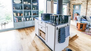 A modern kitchen with a central island, built-in shelving, and a stone wall. - The Barn (Riding Mill)