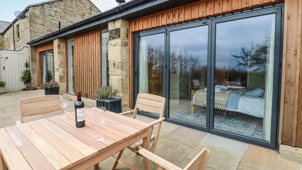 A wooden patio with a table and chairs, a wine bottle, and a potted plant. - The Barn (Riding Mill)