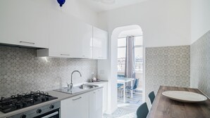 A modern kitchen with white cabinets, a gas stove, and a sink. There is a dining area with a wooden table and chairs. - B&B Damagi (Rome)