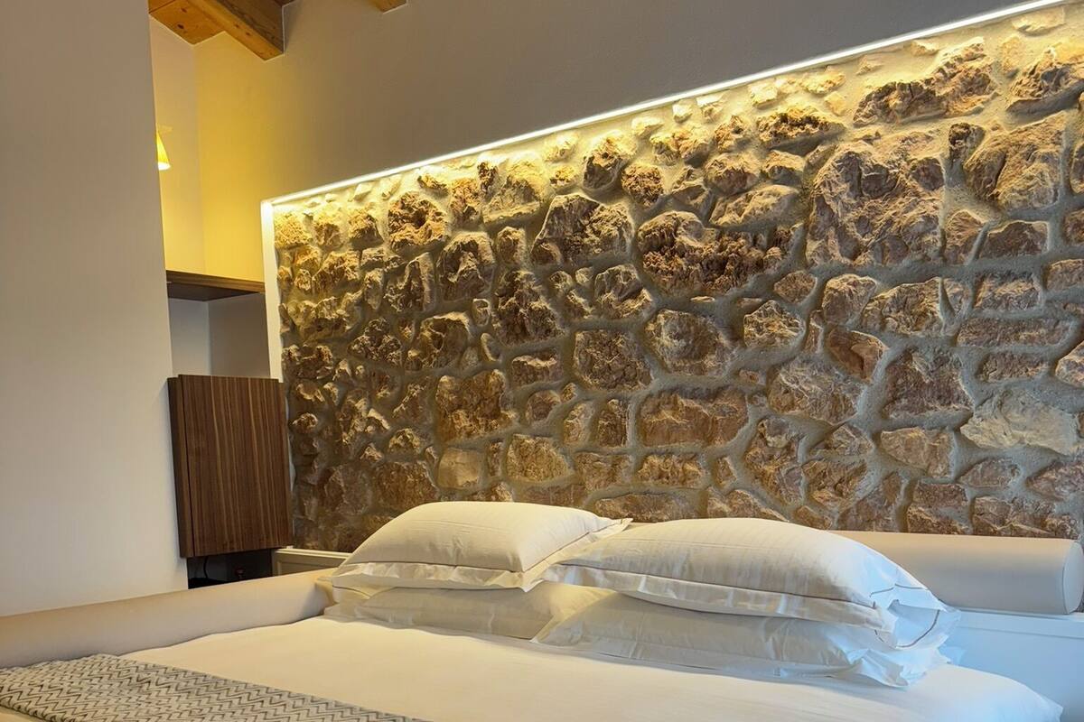 A bedroom with a stone headboard, a bed with white linens, and a patterned throw blanket.