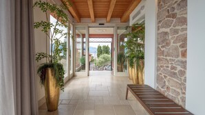 Un pasillo con un banco, plantas grandes en macetas y una pared de piedra.