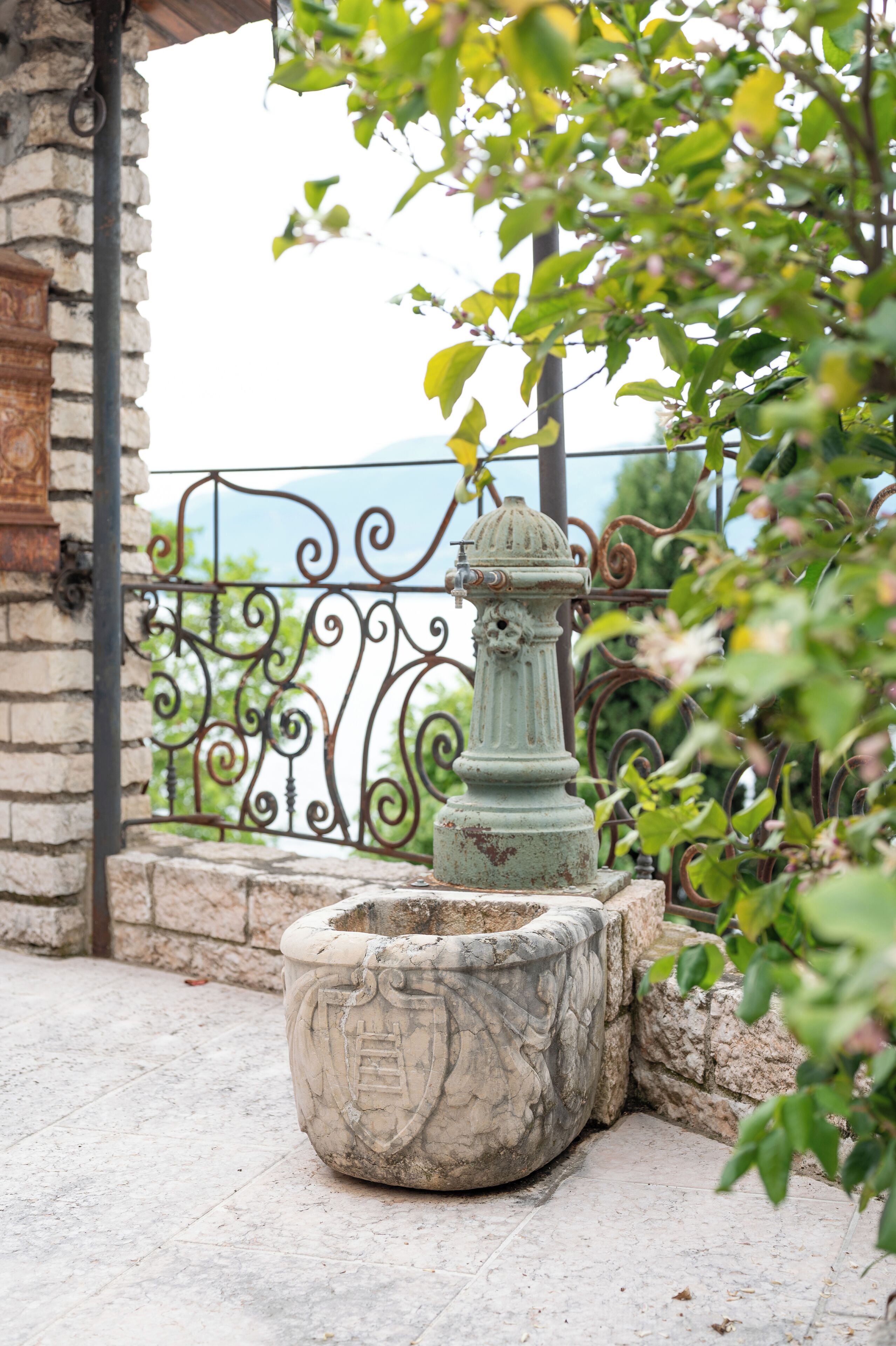 A stone planter with a metal fire hydrant, a wrought iron fence, and a stone wall.