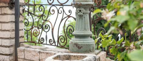 A stone planter with a metal fire hydrant, a wrought iron fence, and a stone wall.
