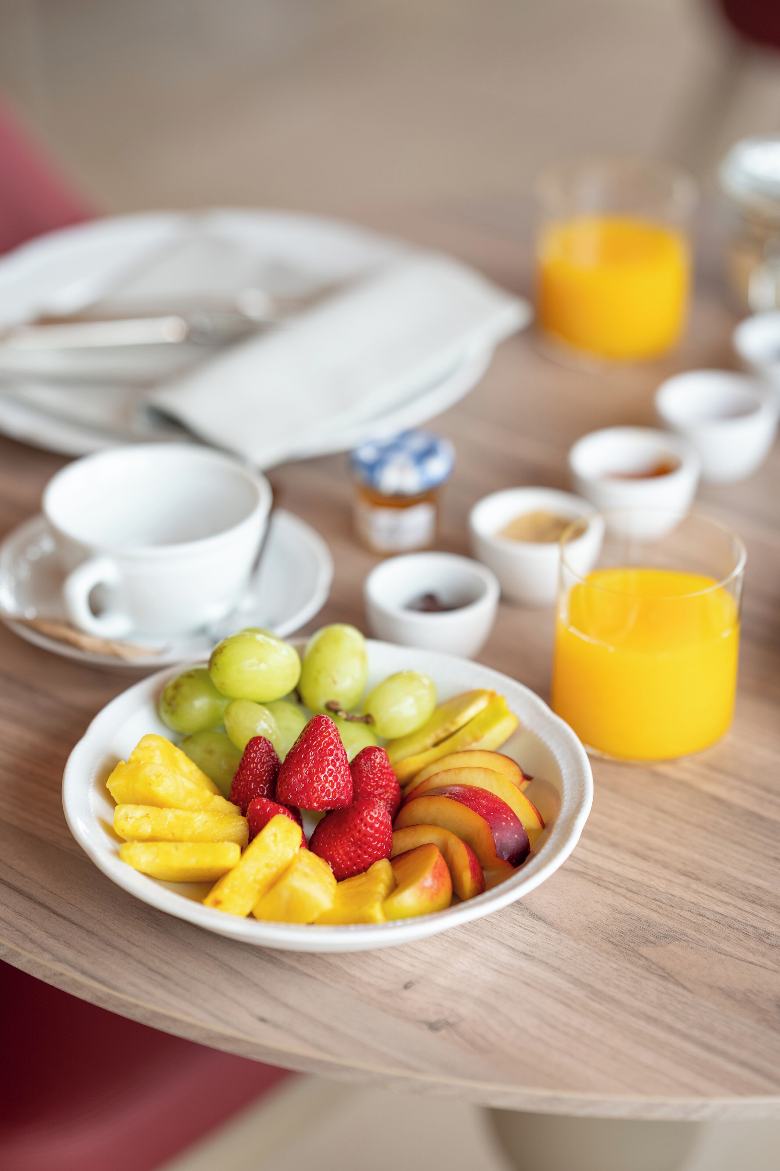 Une table de petit-déjeuner avec un saladier de fruits, un verre de jus d’orange et de petites tasses de café et de thé.