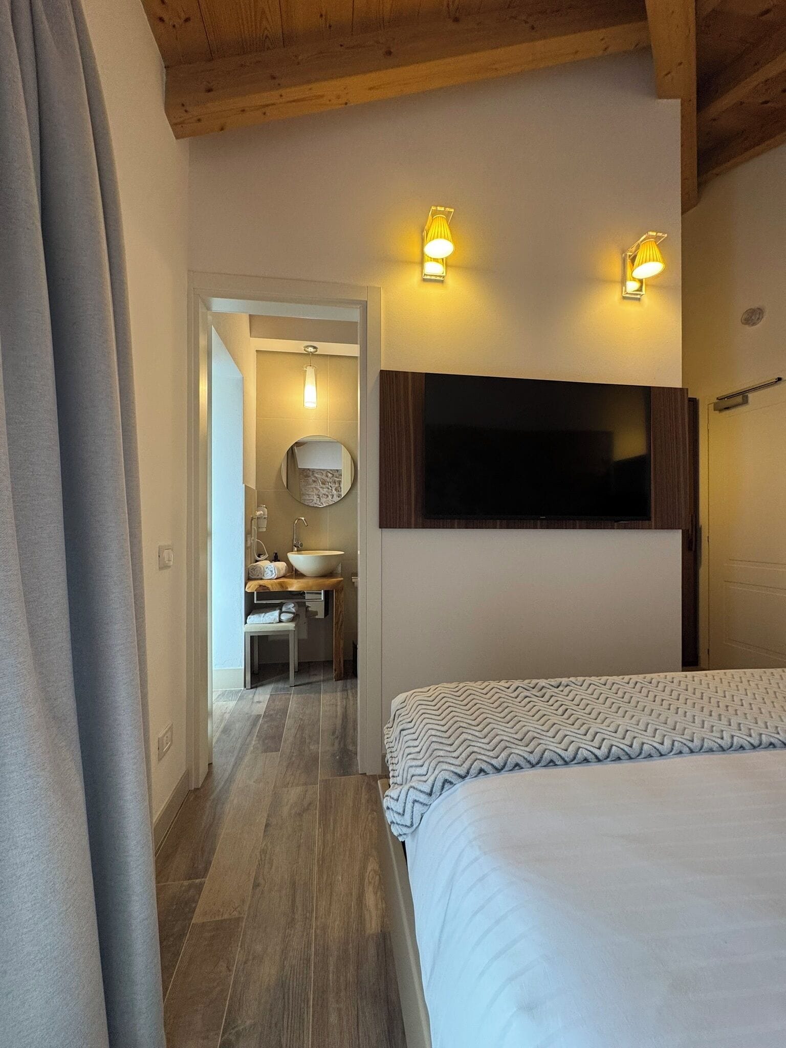 Una camera da letto con un letto, una TV a muro e un bagno visibile attraverso una porta aperta.