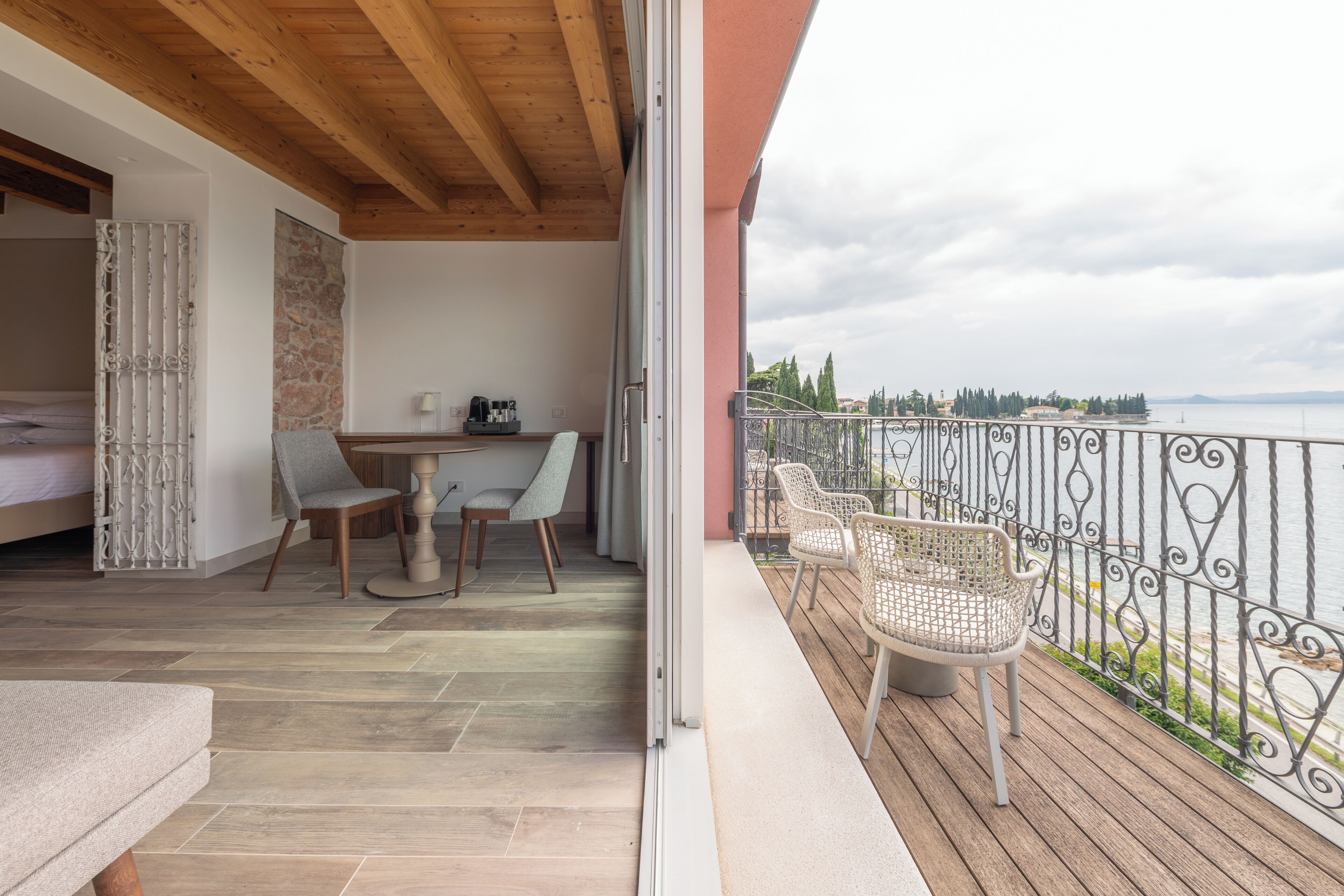 Un balcón con vista al mar, un comedor con mesa y sillas, y una habitación separada con cama y un muro decorativo.