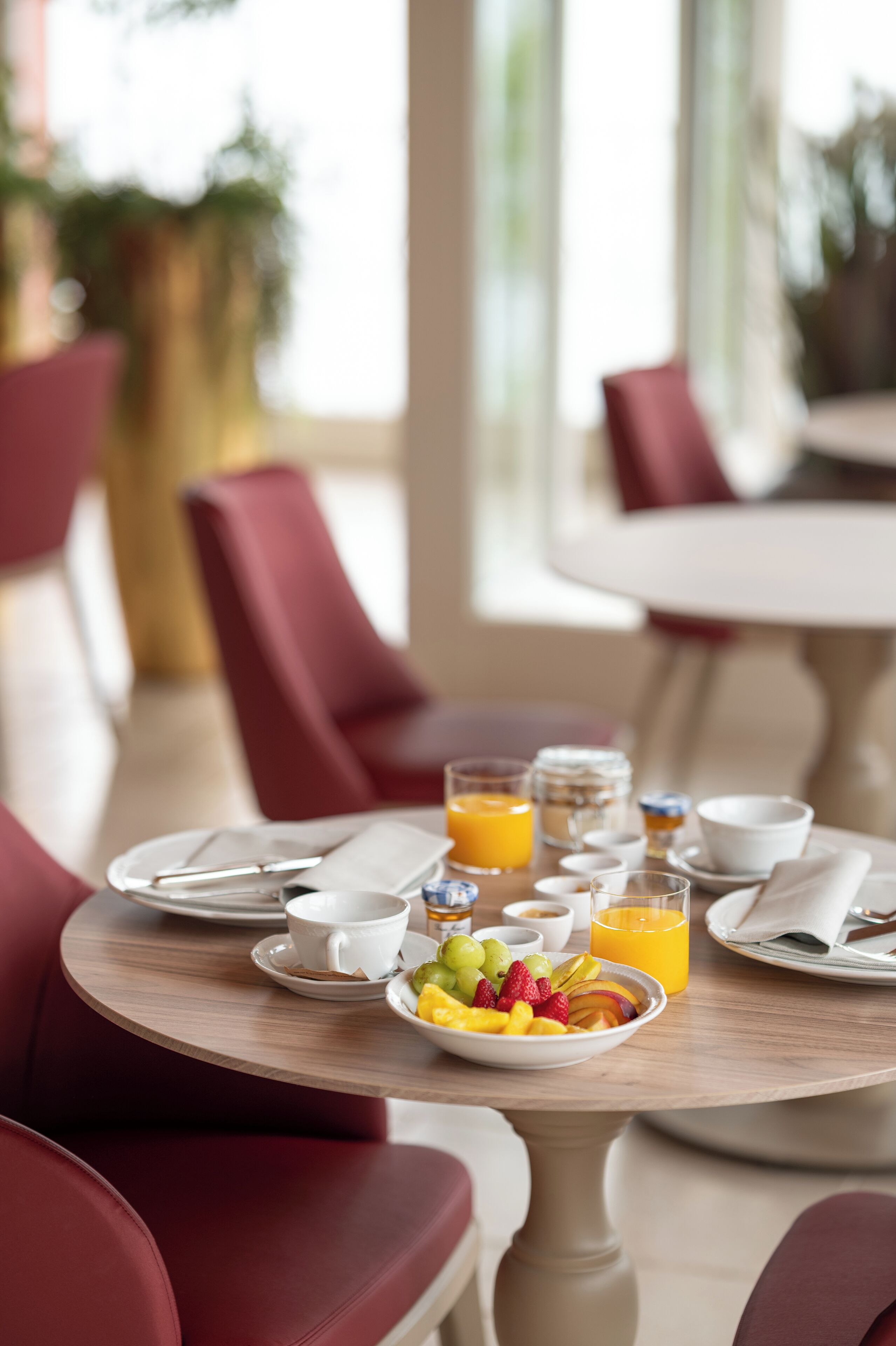 A breakfast setting with a table set for two, including plates, cups, and a bowl of fruit.