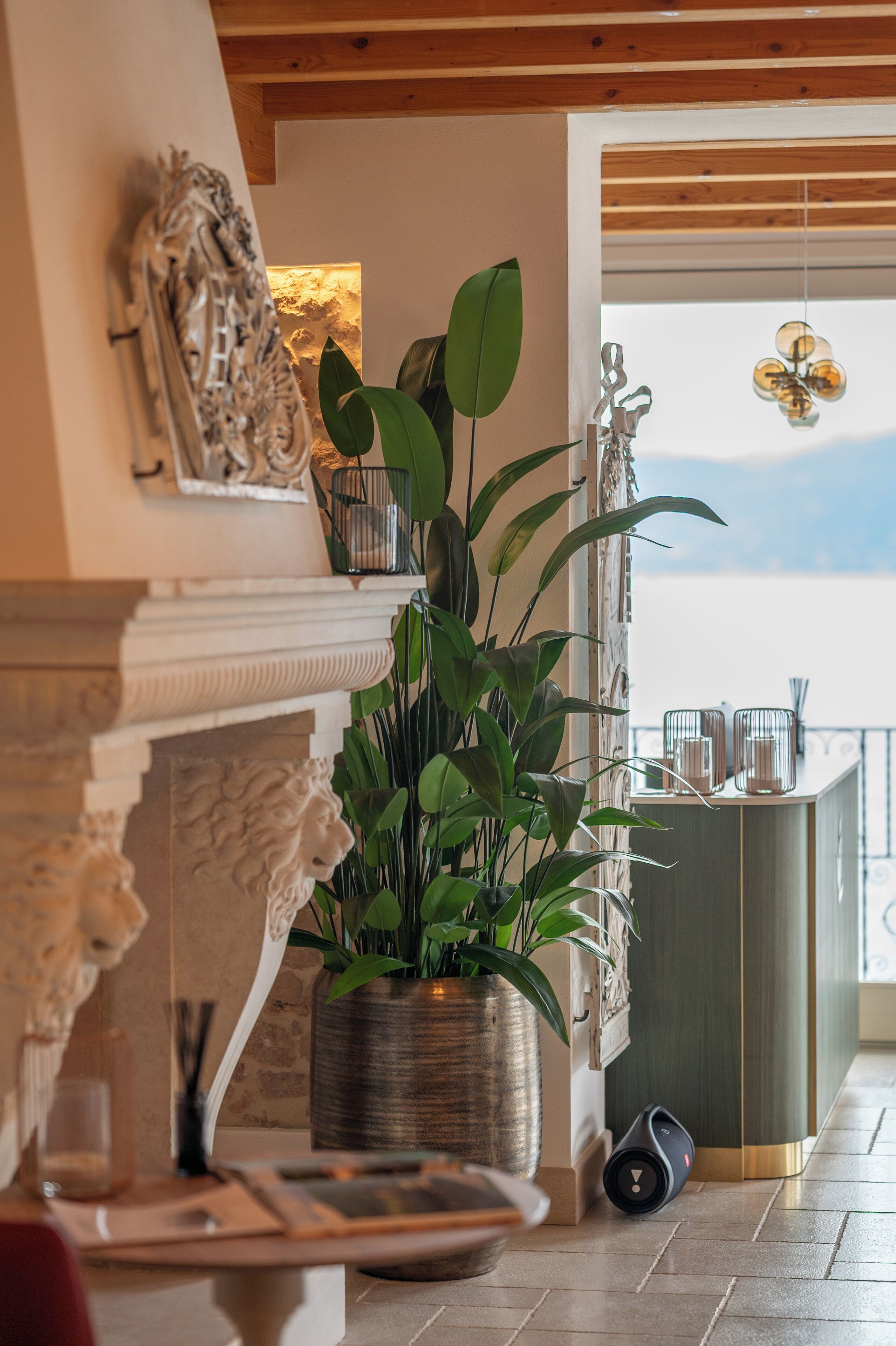 A modern living room with a fireplace, a large potted plant, and a view of the sky through a balcony door.