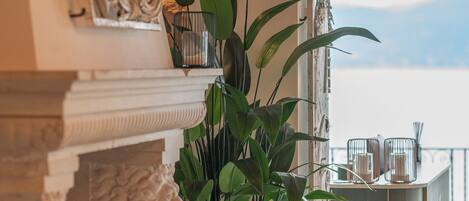 A modern living room with a fireplace, a large potted plant, and a view of the sky through a balcony door.