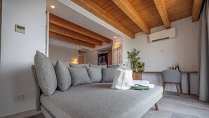 Una sala de estar moderna con un sofá gris, vigas de madera en el techo y un equipo de aire acondicionado, además de un comedor con mesa y sillas.