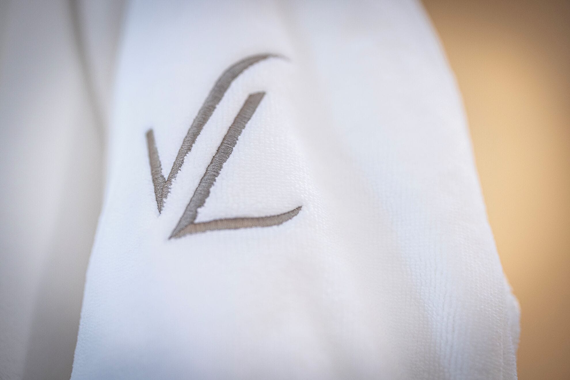A close-up of a white fabric with a stylized 'V' embroidered on it.