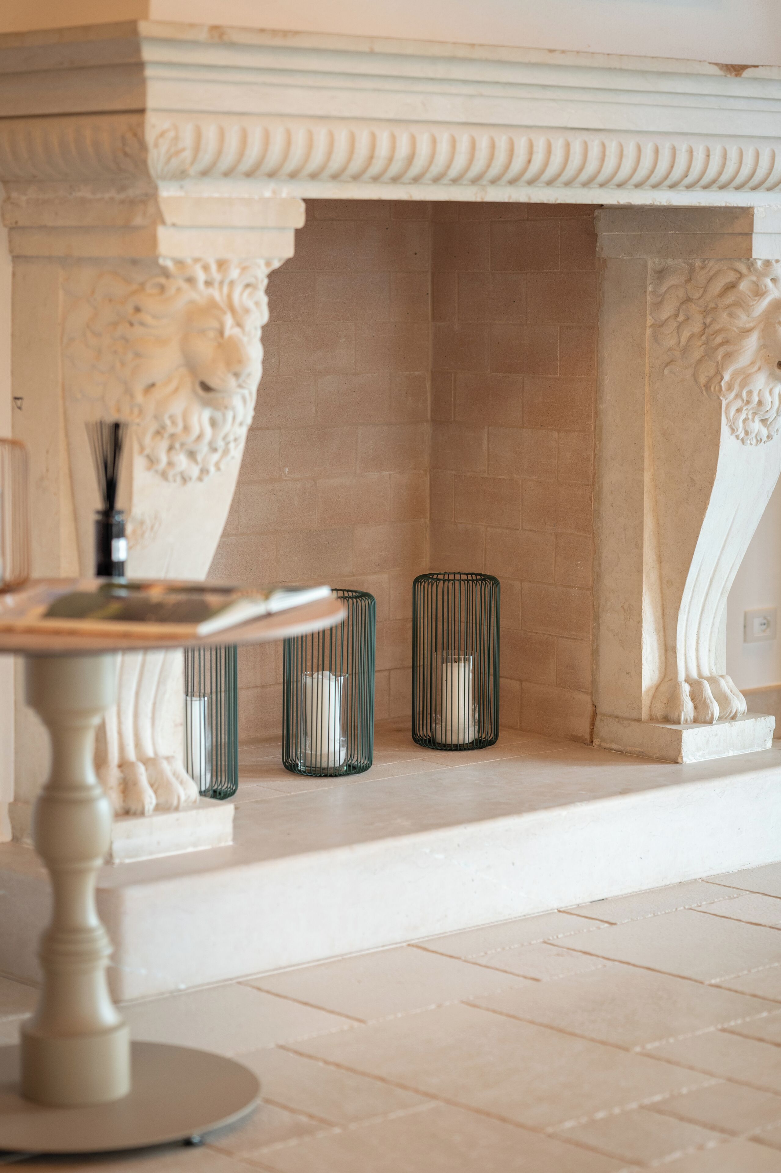 Una chimenea de mármol con una escultura de león, una mesa redonda y dos candelabros.