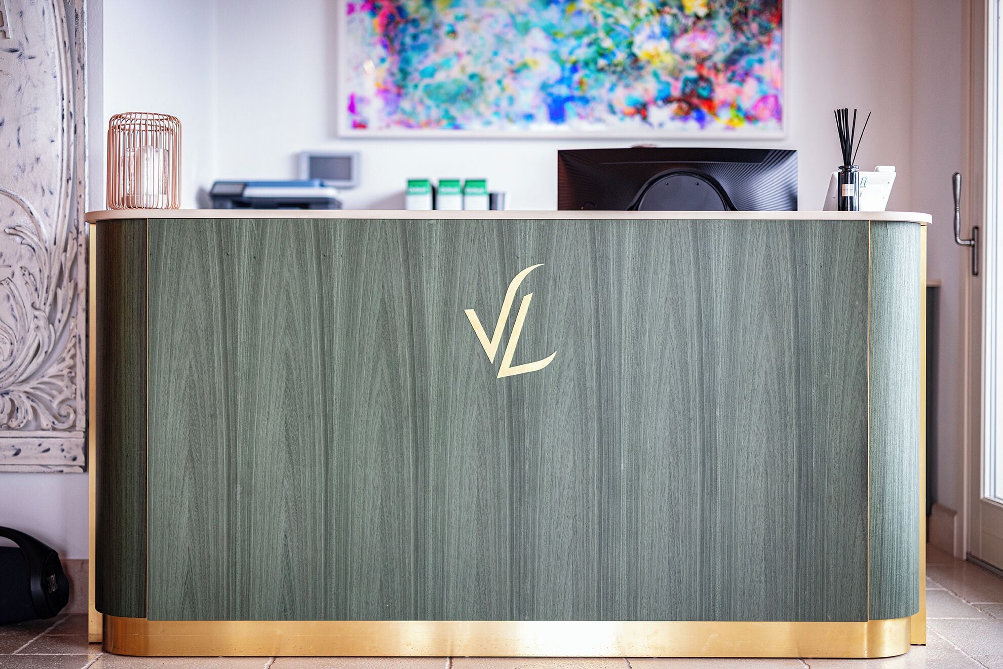 A reception desk with a green textured surface and a gold border. A logo is visible on the desk.