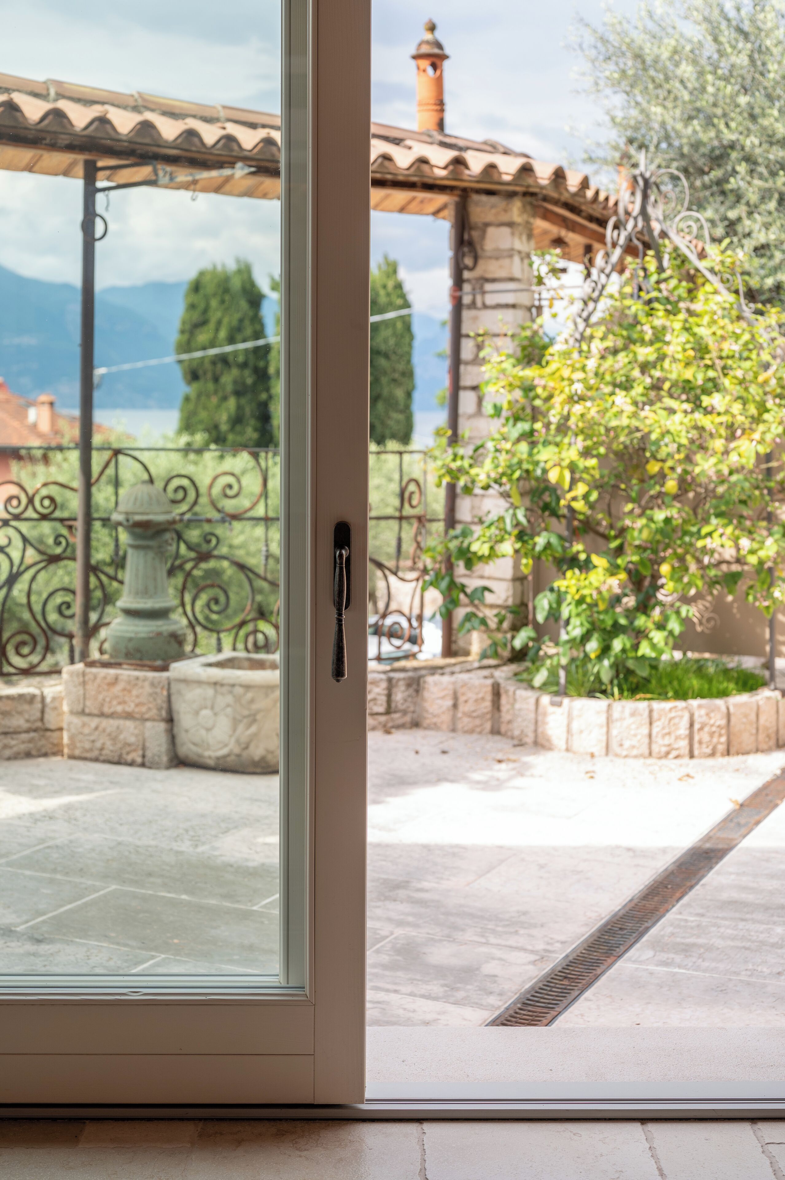 A glass door leading to an outdoor patio with a stone balustrade, a metal fence, and a view of distant mountains.