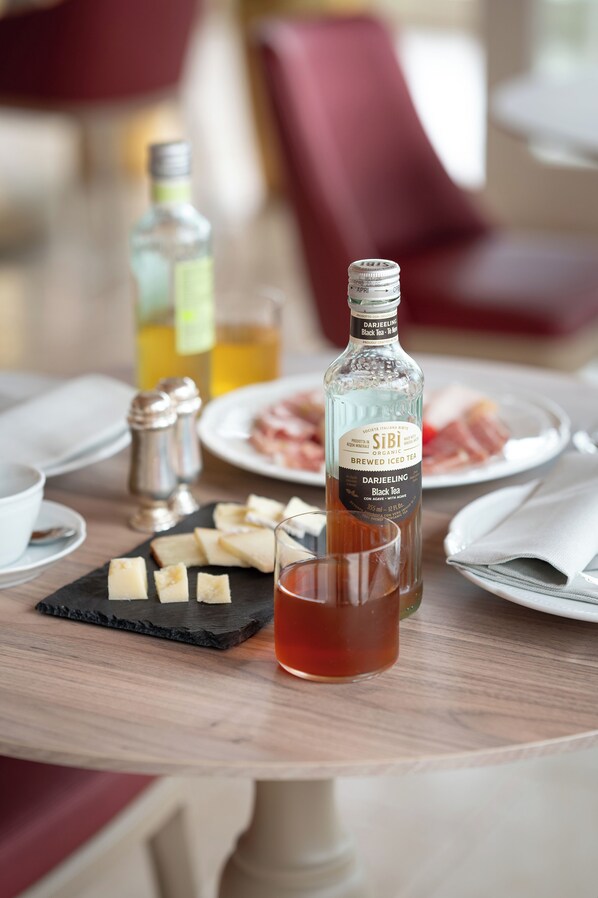 A table with a bottle of Darjeeling Black Tea, a glass of tea, cheese, and plates of food.