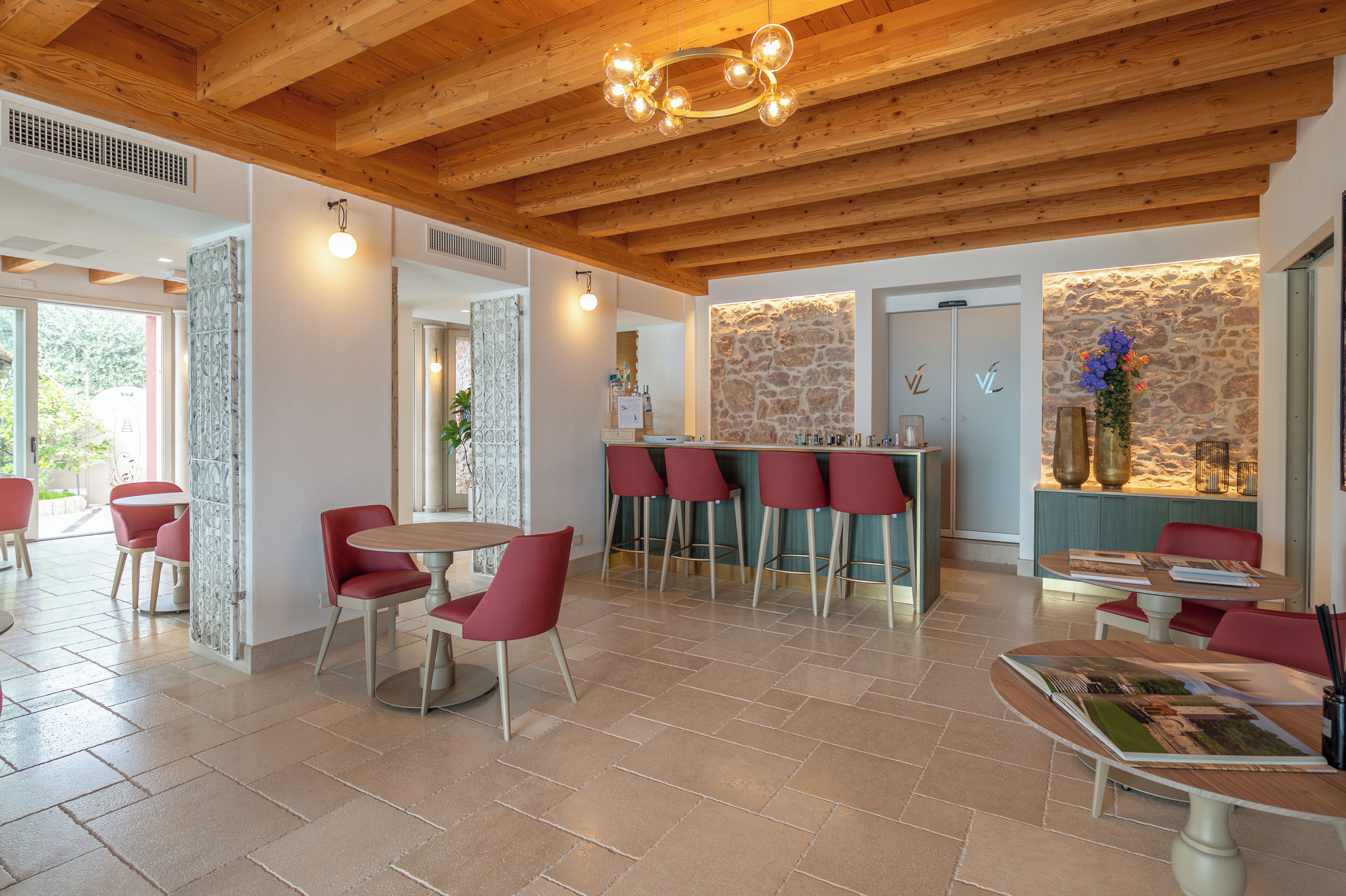 A modern interior with wooden beams, a stone wall, and red chairs around tables.