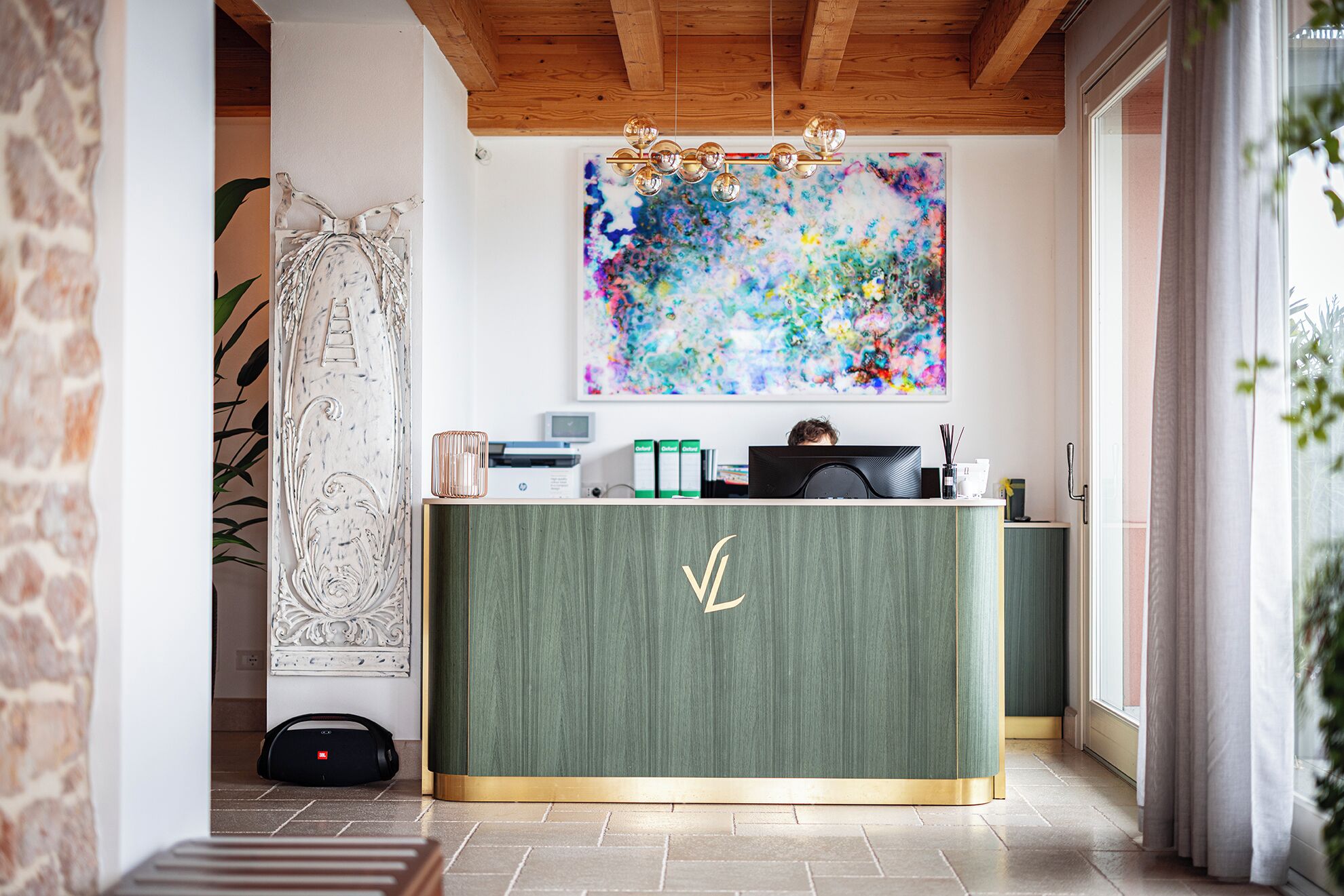 Una reception con decorazioni verde e oro, un quadro astratto colorato sopra e una persona seduta dietro.