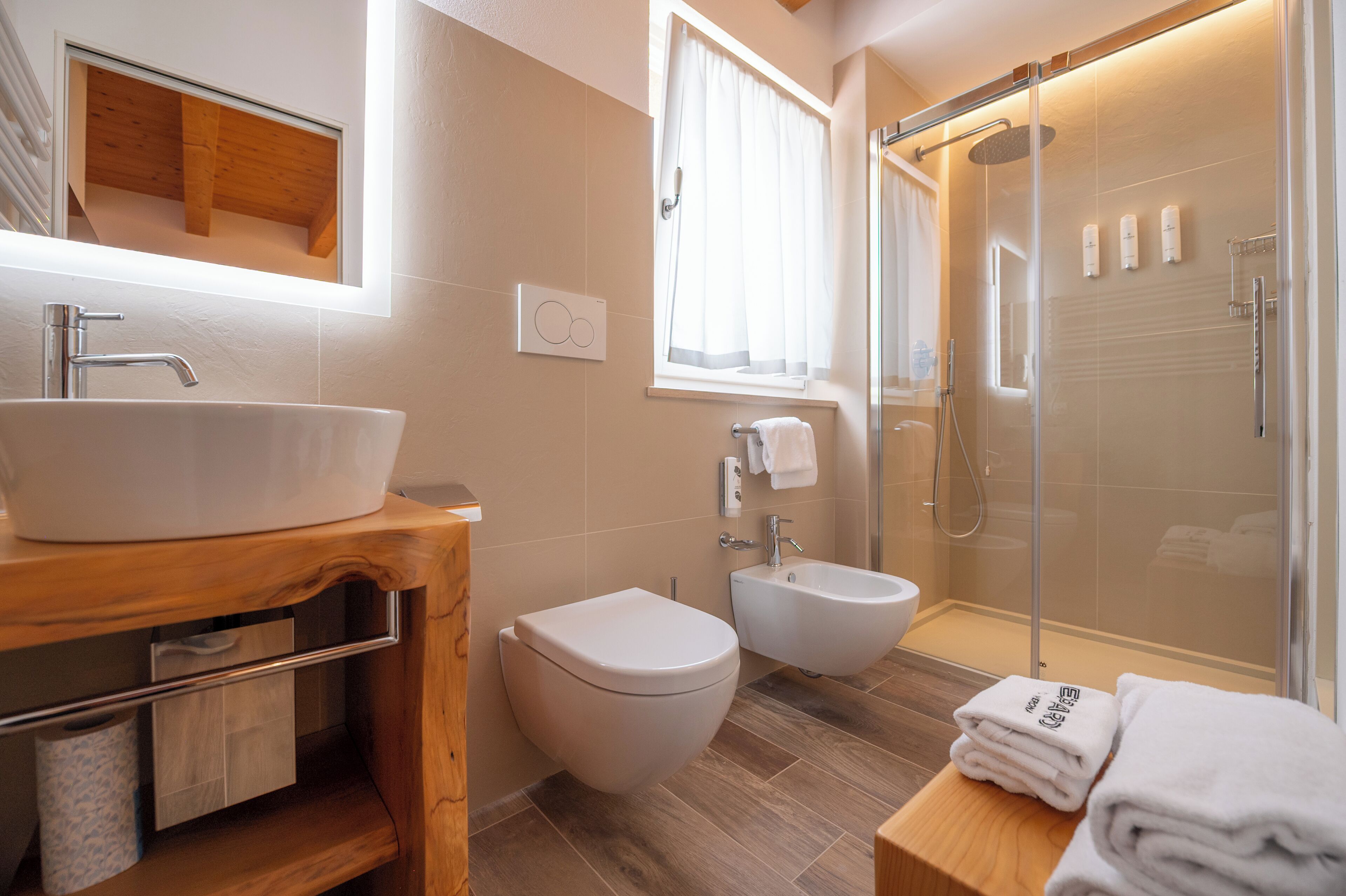 A modern bathroom with a large sink, a bidet, a glass-enclosed shower, and a wooden vanity.