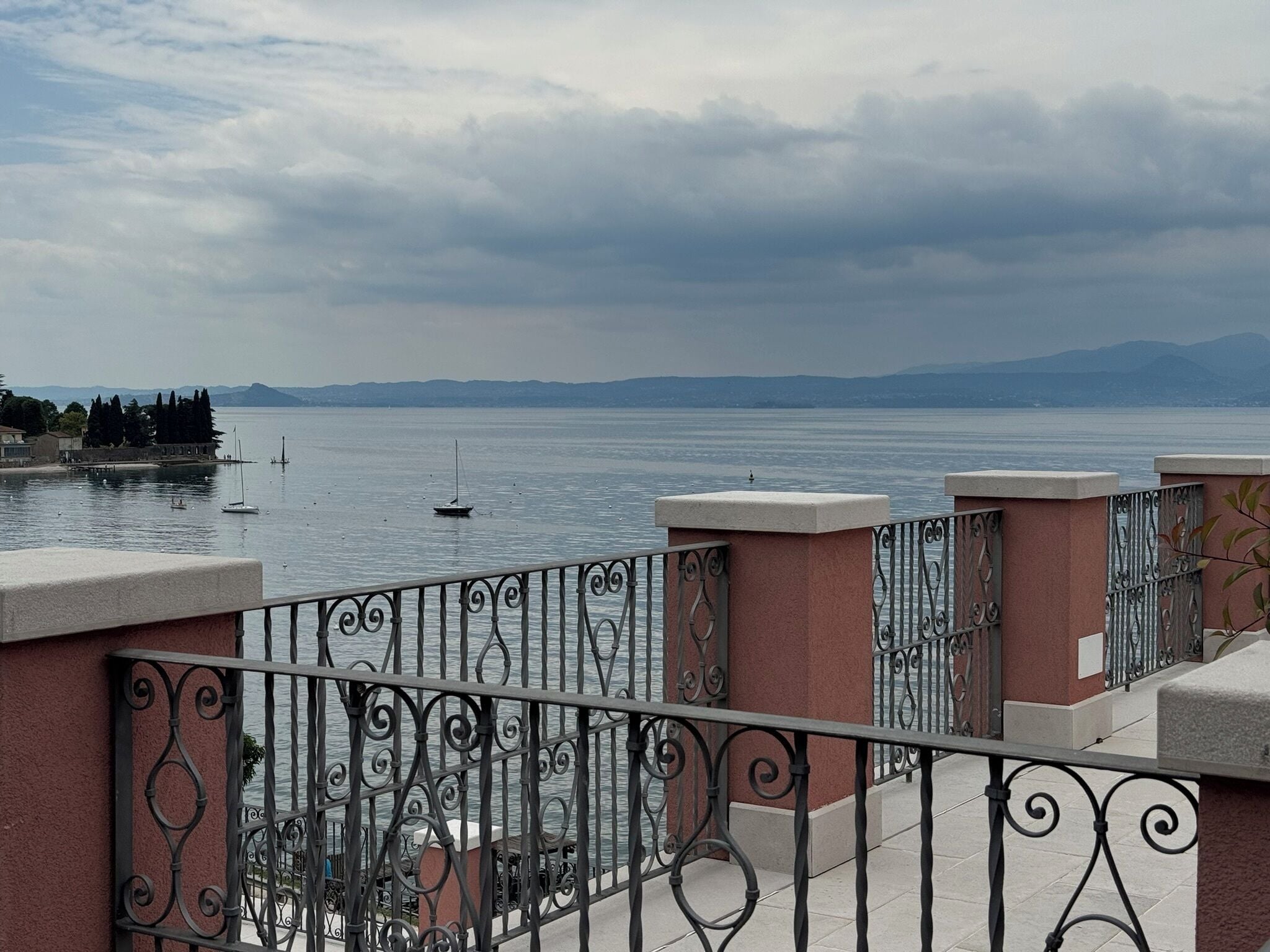 A balcony with wrought iron railings overlooking a calm body of water with boats.