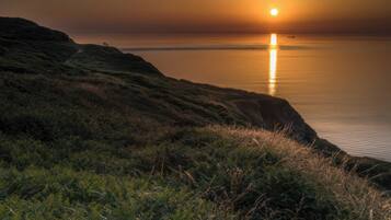 A coastal landscape with a sunset, cliffs, and a calm sea.