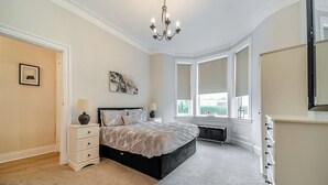 Un dormitorio con una cama grande, un aparador, una mesita de noche con lámparas, una araña y una ventana con vistas a zonas verdes.
