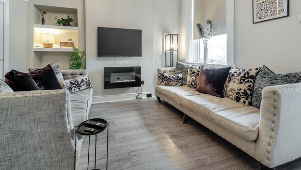 Una sala moderna con sofá, sillones, televisor y candelabro.