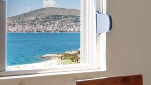Una habitación con ventana que da a una ciudad costera, una silla de madera y una mesa.