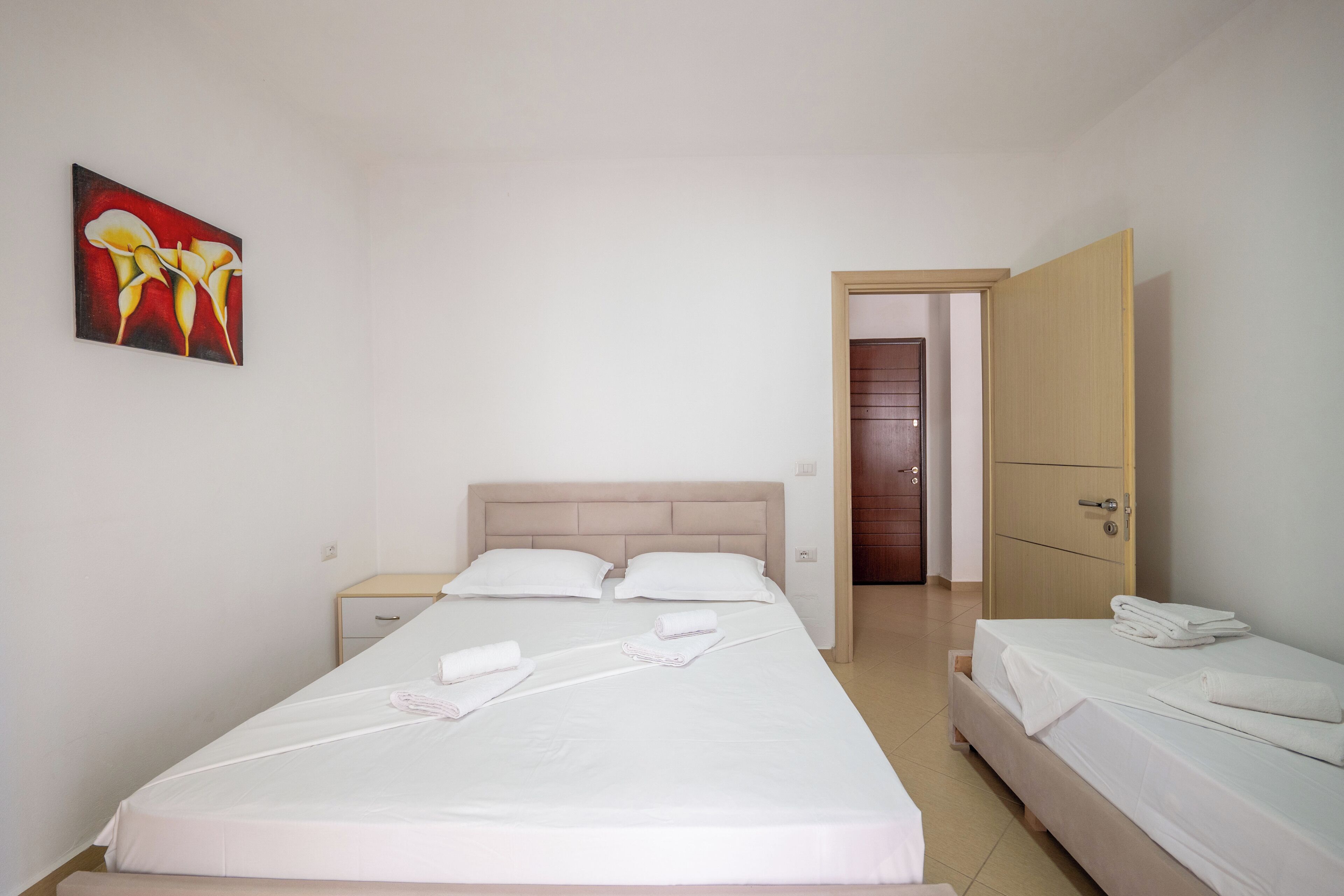 A hotel room with a large bed, a bedside table, a wardrobe, and a painting on the wall.