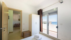 Habitación de hotel con cama, armario, mesita de noche pequeña y vista al mar a través de una puerta corrediza.