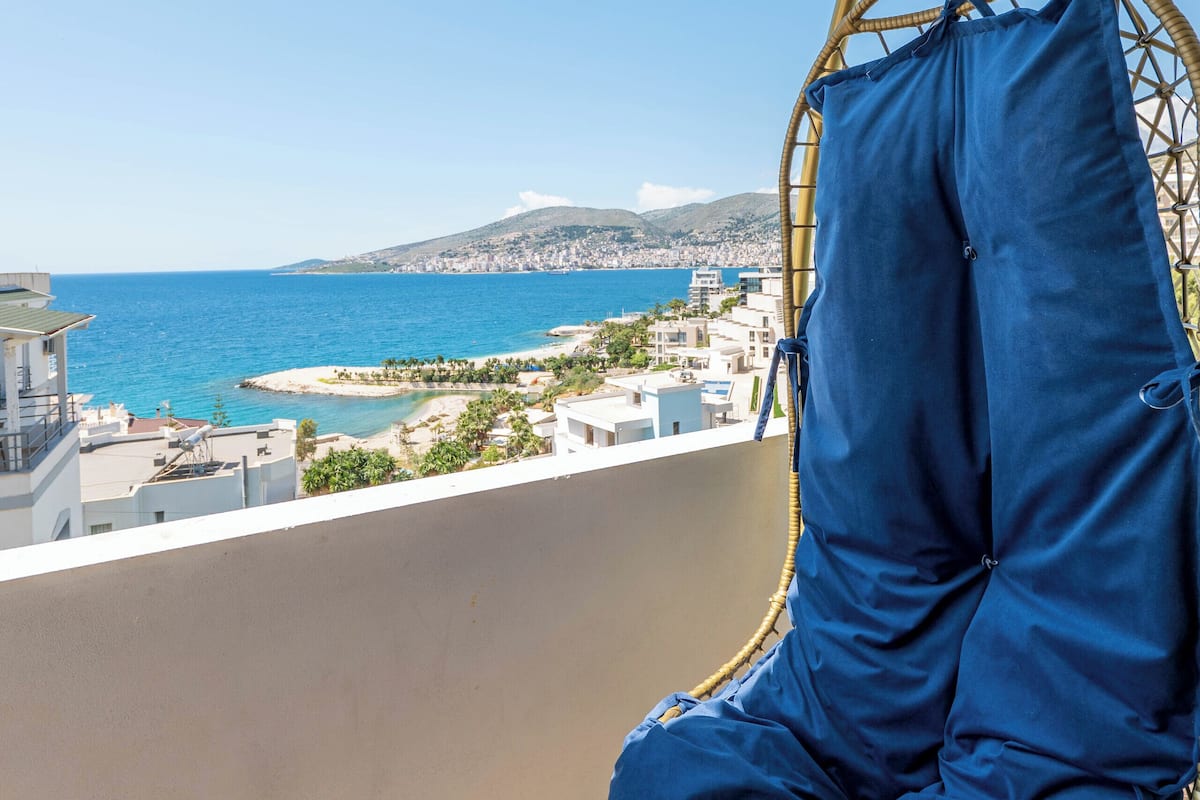 Ein Balkon mit Korbstuhl und Blick auf das Meer und die Stadt.