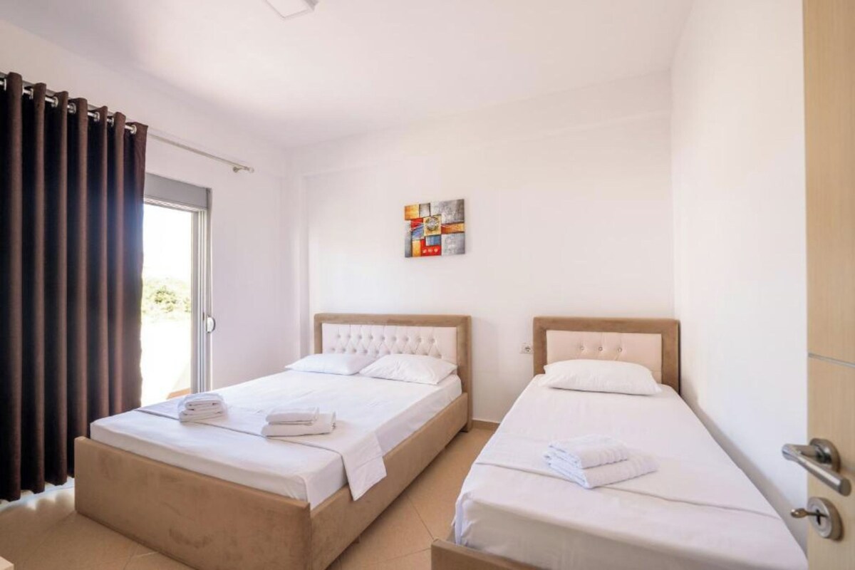 A hotel room with two beds, a door, and a window with curtains.