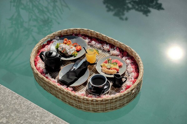 Un montaje para comer flotando, con platos de comida, una bebida y una cafetera sobre el agua.