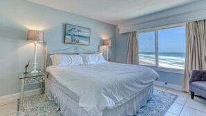 A spacious bedroom with a large bed, a view of the ocean, and a window with curtains.