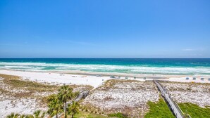 A beach with a wooden boardwalk leading to the shore, clear skies, and calm ocean waves.