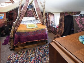 A four-poster bed with a colorful blanket, a wooden dresser, and a patterned rug in a room with floral wallpaper and a skylight. - 2 bedroom accommodation in Walney, near Barrow-in- Furness (Walney, near Barrow-in- Furness)