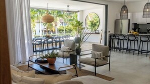 Una sala de estar moderna con sofá, sillas, una zona de comedor y una cocina con taburetes de bar.