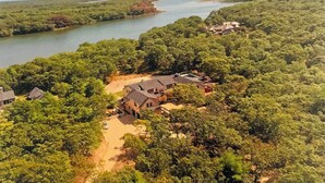 A large house surrounded by dense forest, with a river in the background. - Brand New Spacious Luxury Home on Edgartown Great Pond with Pool and Spa (Edgartown)