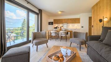 A modern living room with a dining area, a kitchen, and a balcony with a mountain view.