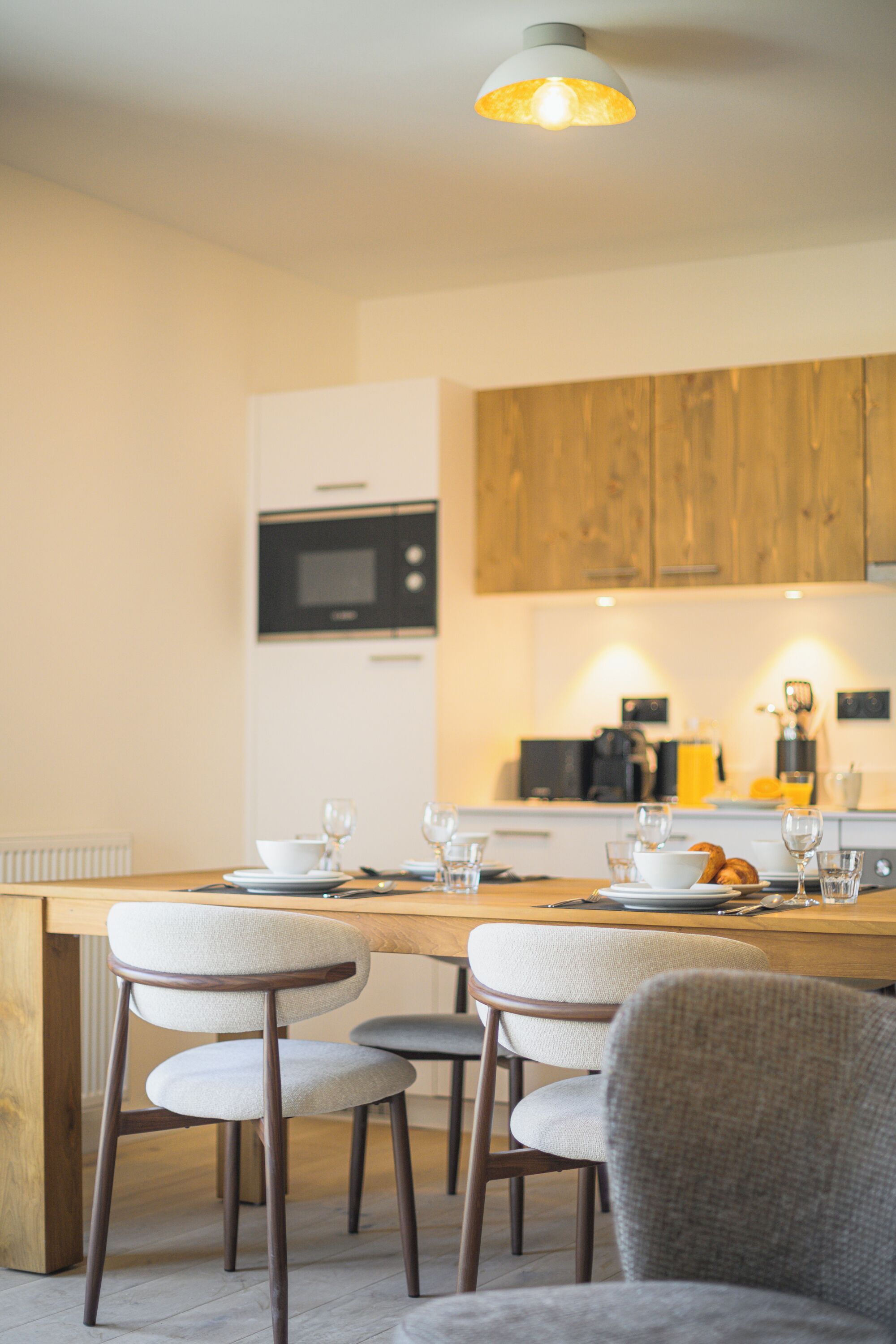 A modern kitchen with wooden cabinets, a built-in microwave, and a dining area with a wooden table and upholstered chairs.
