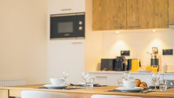 A modern kitchen with wooden cabinets, a built-in microwave, and a dining area with a wooden table and upholstered chairs.