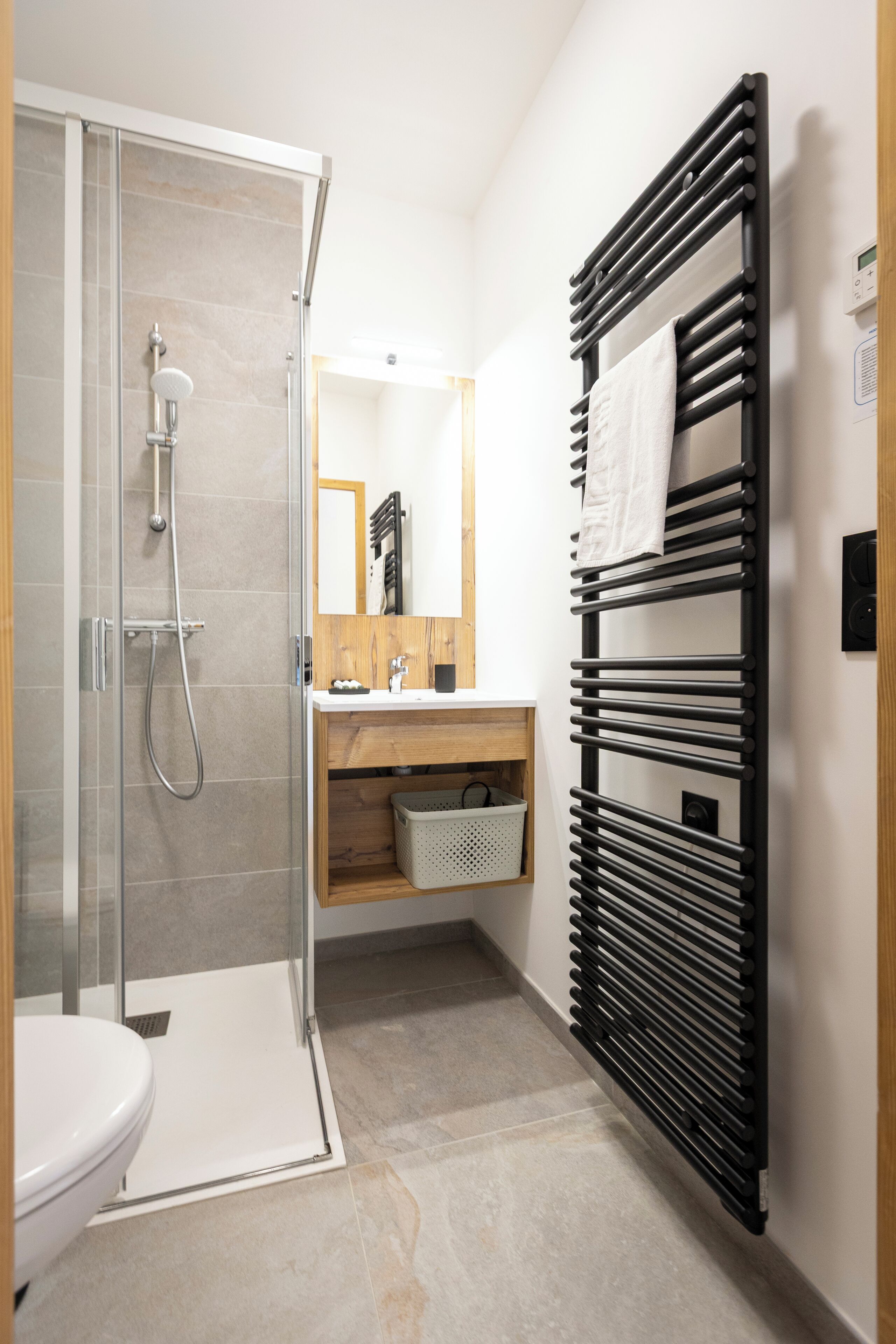A modern bathroom with a glass shower enclosure, a black towel rack, and a wooden vanity.